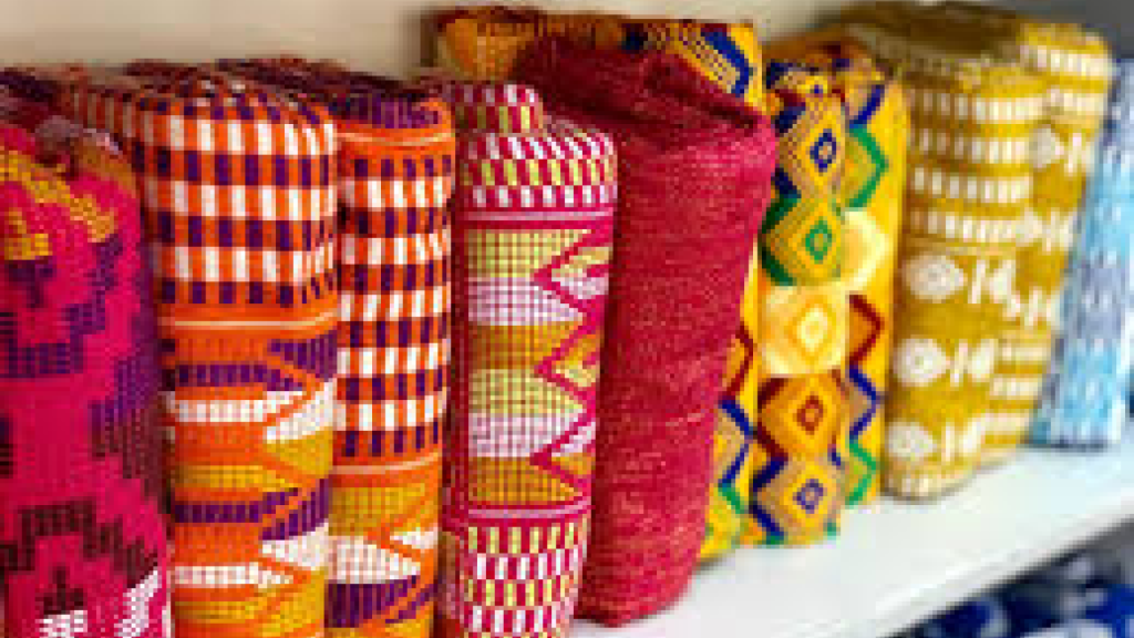 A display of colorful Kente cloth rolls showcasing various traditional patterns and designs, arranged neatly on a shelf.